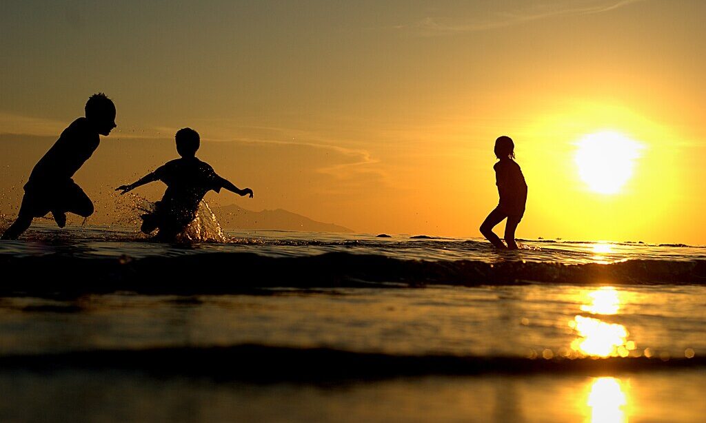 Children at the ocean shore, the sun is beginning to set just above the horizon