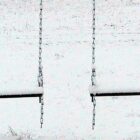 Two snow covered swings on a snowy day.