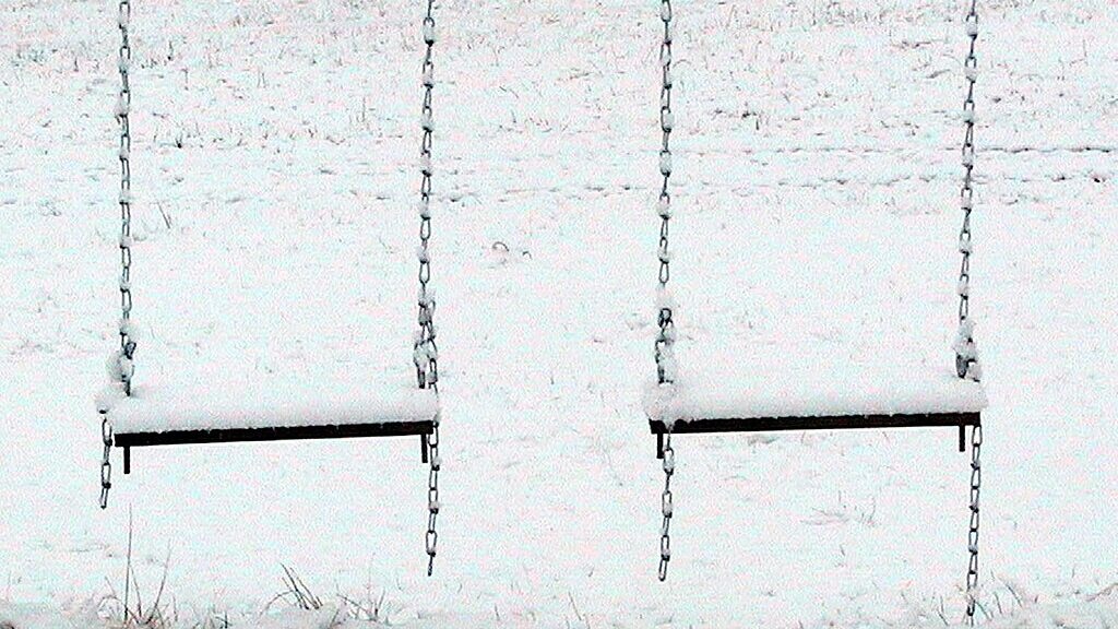 Two snow covered swings on a snowy day.